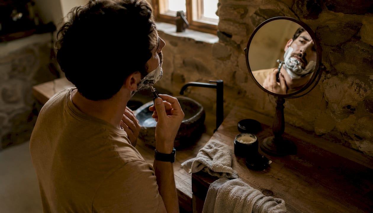 Man carefully shaving beard in bathroom