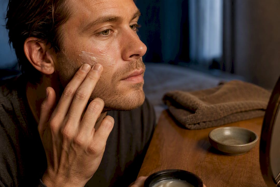 Man applying balm to dry cheek at night